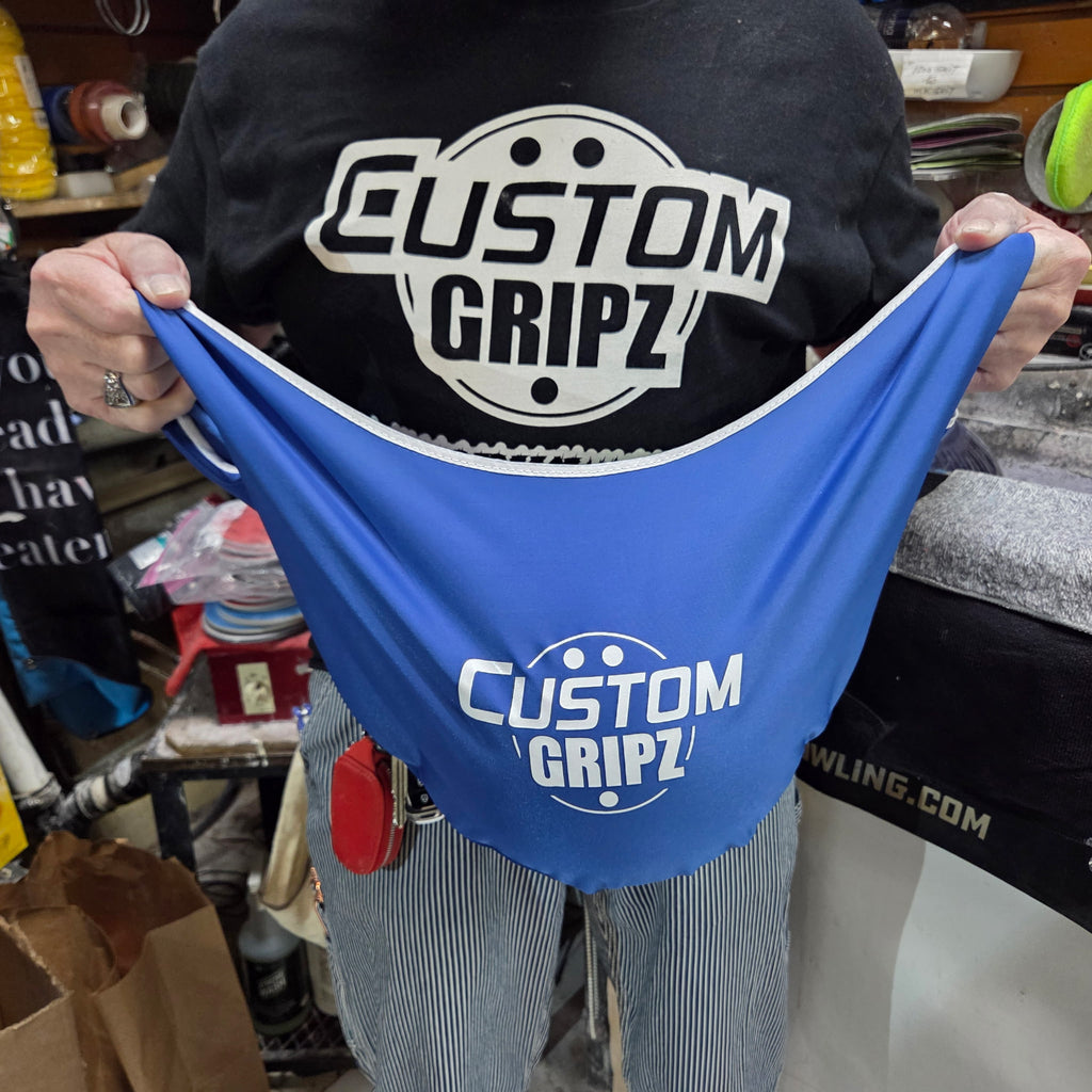 Person wearing a black shirt with 'Custom Gripz' logo holding a blue bowling ball buffer bag with the same logo.